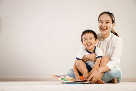 Asian mother and child reading book together concept. Vietnamese mum and son sitting on floor,...