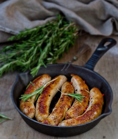 fried sausages on a frying pan on a wooden backgroundの写真素材