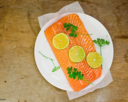 fresh, crude fillet of a salmon with slices of a lime and greens on a wooden background