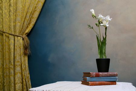 a pot of freesias on top of books beside a yellow curtainの写真素材