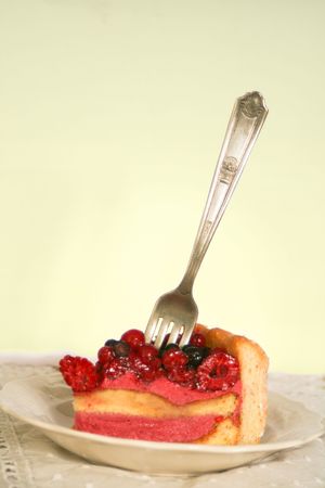Slice of sponge layer cake topped with raspberry, blueberry, and currants with a fork stabbed into it.の写真素材