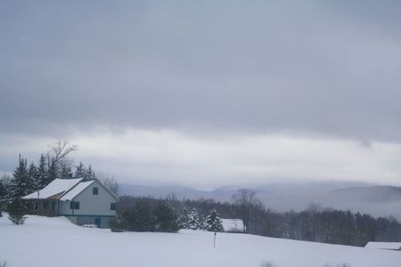 a snow covered farmhouse sitting on a slope overlooking a valley on a stormy dayの写真素材