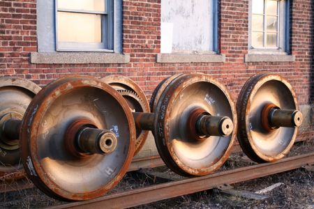 three rusty train axles beside three windows of a brick buildingの写真素材
