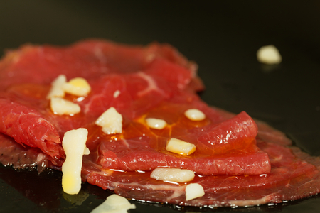 Carpaccio with olive oil and parmesan cheese on a black background.の写真素材