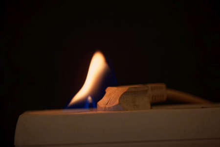 Burning plug socket with a flame and a dark background.の写真素材