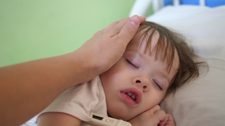 mom measures temperature with thermometer to baby and caresses child with hand. close-up. baby...