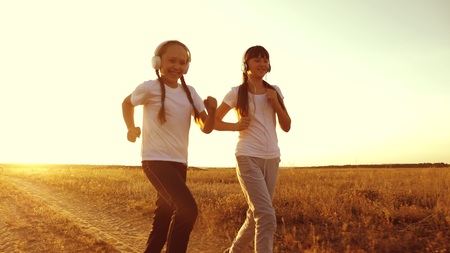 young girls are training at sunset and listening to music. teen girls in headphones doing sports jogging in the countryside.の写真素材