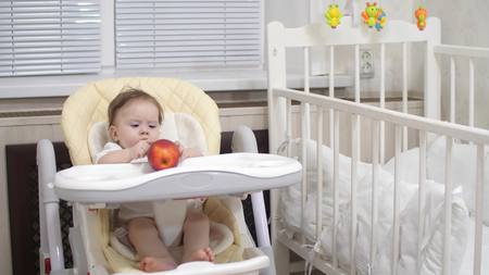 Kid is playing with red apple sitting on chair.