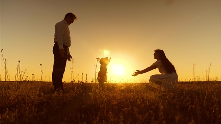 Little daughter goes to her mother in her arms at sunset. Happy mother hugs and kisses baby. Dad, mom and baby are playing for walk in evening. First stepsの写真素材