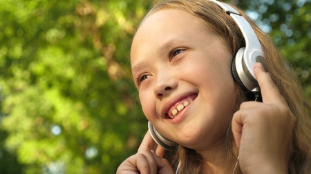 Girl in headphones listening to music and smiling dancing in summer parkの写真素材