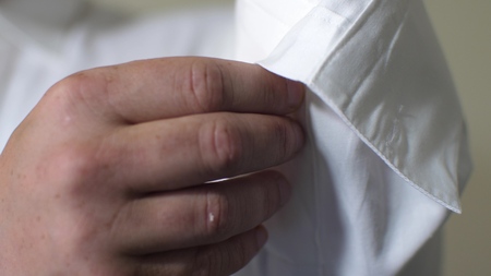 Man businessman puts on white shirt in morning, buttoning his buttons with his hands. Concept business worker. Close-upの写真素材