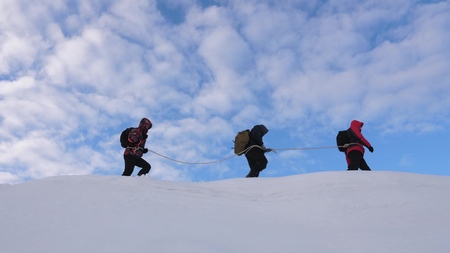 mountaineers tied with rope follow each other along snowy ridge. team of travelers in winter go to top of the mountain. well-coordinated teamwork tourism in winterの写真素材