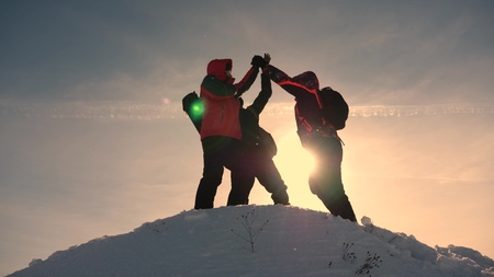 team work and victory. Tourists come to top of snowy hill and rejoice at victory against backdrop of a yellow sunset. teamwork of people in difficult conditions.の写真素材