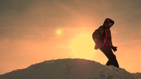 Tourist stands on top of snowy hill in the rays of the bright sun. The traveler descends from the...