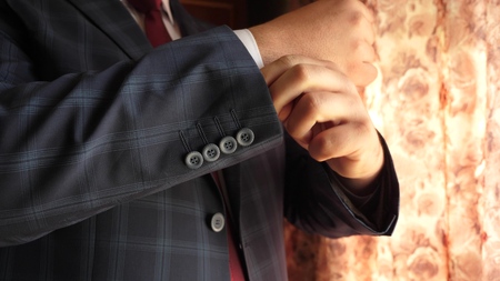 businessman in red tie dark blue check suit straightens sleeve of white shirt. dark blue check suit. office worker gets dressed for work in morning. concept of stylish and fashionable clothes for menの写真素材