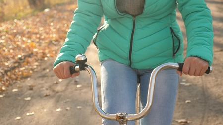 girl holds curved steering wheel and rides a bicycle in autumn park, close-up