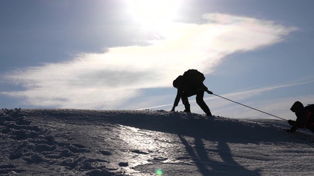 teamwork desire to win. Climbers on a rope help a friend climb to the top of the hill. Silhouette of travelers in winter on a hill in the bright rays of the sun. concept of sports tourism.の写真素材