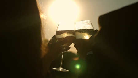 champagne sparkles and foams in sun. couple in love holding wine glasses with sparkling wine on...