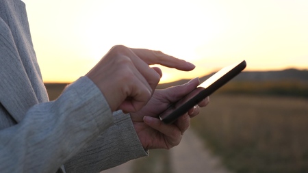 fingers of girl touch screen of tablet, smartphone. close-up. Female hands are holding a tablet and checking emails in the park at sunset. girls hand prints a mobile message on the smartphone screen.の写真素材