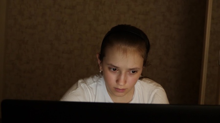 Tired teen girl looks into the screen of a laptop monitor. close-up. A young girl looks at computer screen with tired eyes in her room at night. tired teen girl looks into screen of a laptop monitor.の写真素材