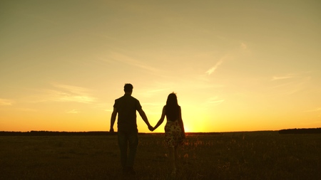 Young couple in love walking across the field holding hands. girl and man go to the sunset. happy family walks in the park in summer in the rays of the sun. happy family conceptの写真素材