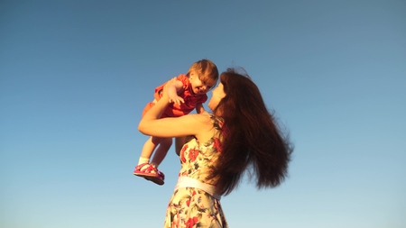 Mom throws her daughter up to the sky. mother plays with a small child against a blue sky. happy family playing in the evening against sky. mother throws up the baby, baby smiles. slow motion filming.の写真素材