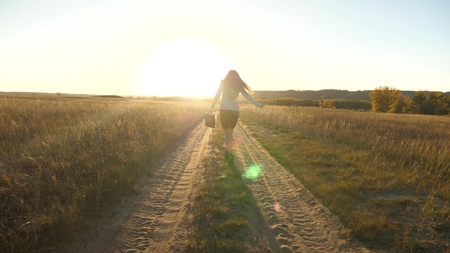 business woman walking along a country road with a briefcase in her hand. sexy business woman girl working in rural area. woman farmer inspects land at sunset. agricultural business concept.の写真素材