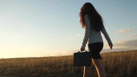 sexy businesswoman girl running in the countryside. business woman walking along a country road with a briefcase in her hand. Woman farmer inspects the land at sunset. The concept of agricultural business.の写真素材