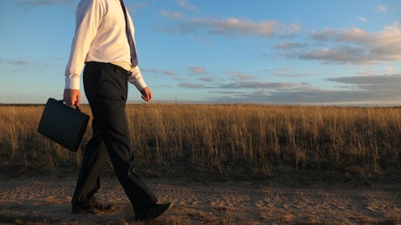 businessman in sunglasses goes down the country road with a briefcase in his hand. The entrepreneur works in a rural area. a farmer inspects the land at sunset. agricultural business concept.の写真素材