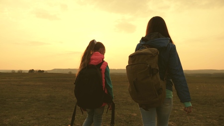 Mom and daughter travel with a backpack against the sky. tourists mother and child go to sunset in the mountains. happy family on vacation travels. sports tourism concept.の写真素材