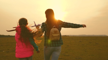 children play toy airplane. Happy girl sisters run with a toy plane at sunset on the field. The concept of a happy family. Girls dream of flying and becoming a pilot. Slow motionの写真素材