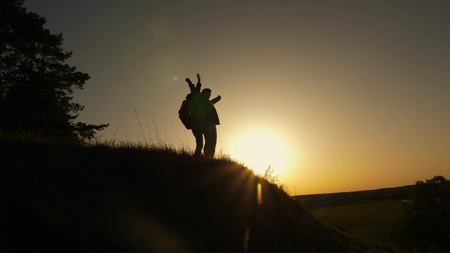 Hiker Girl Raising Her Hand Up, Celebrating Victory And Enjoying Scenery. mom and daughter on vacation traveling and dancing on mountain. Woman with raised hands on top of mountain looking at sunset.の写真素材