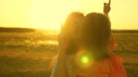 happy mother walks with her daughter in her arms in the rays of the sunset. Mom is talking with happy baby, baby is sitting on mothers arms at sunset of the golden sun. Slow motion.の写真素材
