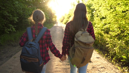 Hiker Girl. girls travel with backpacks on a country road. women tourists go to the sunset. Happy...