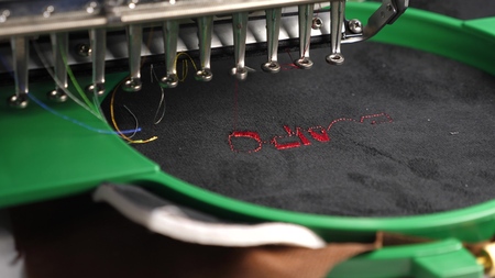 an automated machine embroiders pattern with red threads on a black cloth. Robotics works in tailoring production line. Robot sewing machine. automatic sewing machine. computer controls sewing machineの写真素材