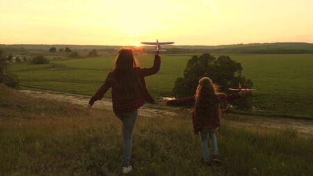 Dreams of flying. Happy childhood concept. Two girls play with a toy plane at sunset. Children on...