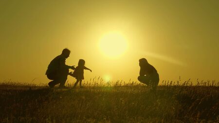 mom and dad play with their little daughter. happy child goes from father to mother. mother and Dad play with their daughter in sun. young family with a child of 1 year. family happiness concept.の写真素材