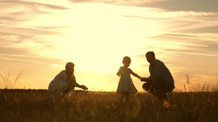 Mom and Dad playing with their daughter in park at sunset. kid takes the first steps. Happy family playing with the child in the rays of sun. baby goes from dad to mom and laughs. Slow motion.の写真素材