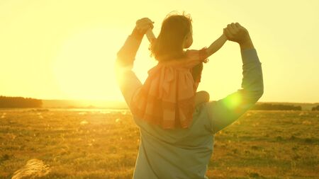 Dad dancing on his shoulders with his daughter in sun. Father travels with baby on his shoulders in rays of sunset. A child with parents walks at sunset. happy family resting in park. family conceptの写真素材