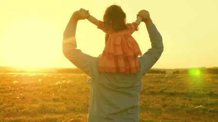 Dad dancing on his shoulders with his daughter in sun. Father travels with baby on his shoulders in rays of sunset. A child with parents walks at sunset. happy family resting in park. family conceptの写真素材