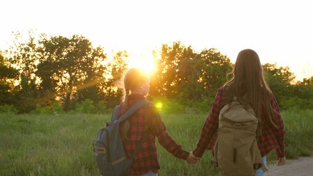 tourist girls on country road. Hiker Girl, teen girls travel and hold hands. children travelers. girls with backpacks are on country road in sun. concept of sports tourism and travelの写真素材