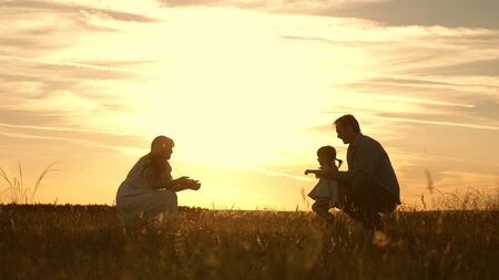 Mom and Dad playing with their daughter in park at sunset. kid takes the first steps. Happy family playing with the child in the rays of sun. baby goes from dad to mom and laughs. Slow motion.の写真素材