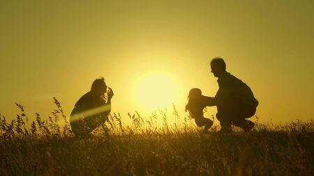 Little daughter with parents jumping at sunset. Silhouettes of mom dad and baby in the rays of dawn. Family concept. Walking with a small child in nature.の写真素材