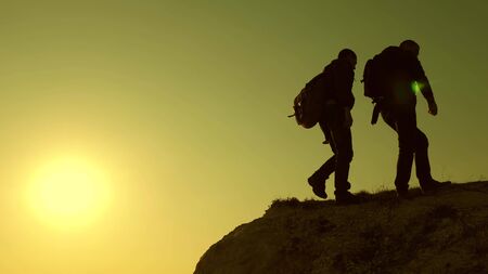 Climbers silhouettes stretch their hands to each other, climbing to top of hill. teamwork of...