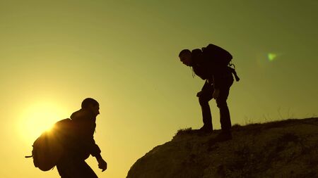Climbers silhouettes stretch their hands to each other, climbing to top of hill. teamwork of business people. travelers climb one after another on rock. team of businessman is going to win.の写真素材