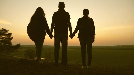 Woman, man and child travel, enjoy scenery at sunset, raise hands up. Freedom. Travelers family travel with backpacks. Happy family of tourists on vacation travel holding hands. Hiker Girl. Teamwork.の写真素材