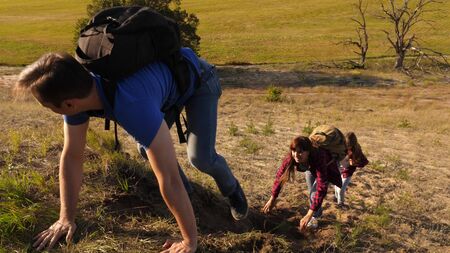father holds out his hand helping children climb mountain. Family of tourists with kids traveling at sunset. dad, children and mom with backpacks travel climb mountain in the sun. tourist teamworkの写真素材