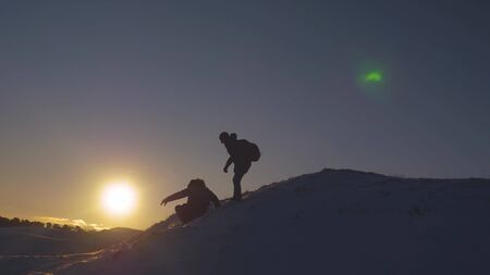 Silhouettes of men descending from high snowy mountain seeking adventure in glare of setting sun in winter. Concept of climbers who conquered mountain.Teamwork. Friends visiting terrain of mountainsの写真素材