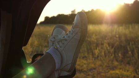 Legs of a girl in a car window, glare of the sun, riding a car on a country road. a young woman likes to travel in a car, putting her legs out of an open window.の写真素材