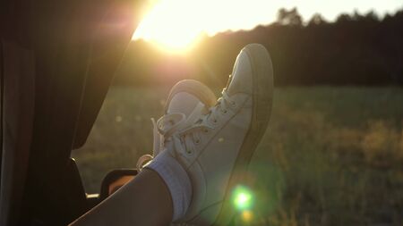Legs of a girl in a car window, glare of the sun, riding a car on a country road. a young woman likes to travel in a car, putting her legs out of an open window.の写真素材